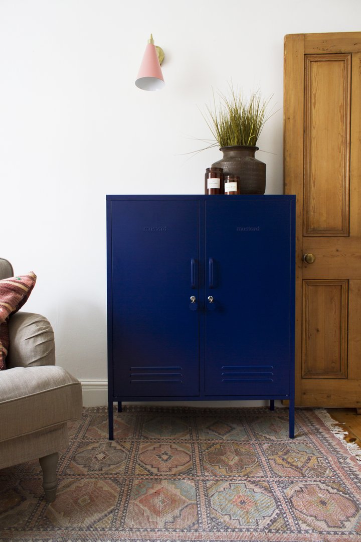 Mustard Made The Midi Locker in nay with a plant ontop sitting on a rug beside a cough and a door