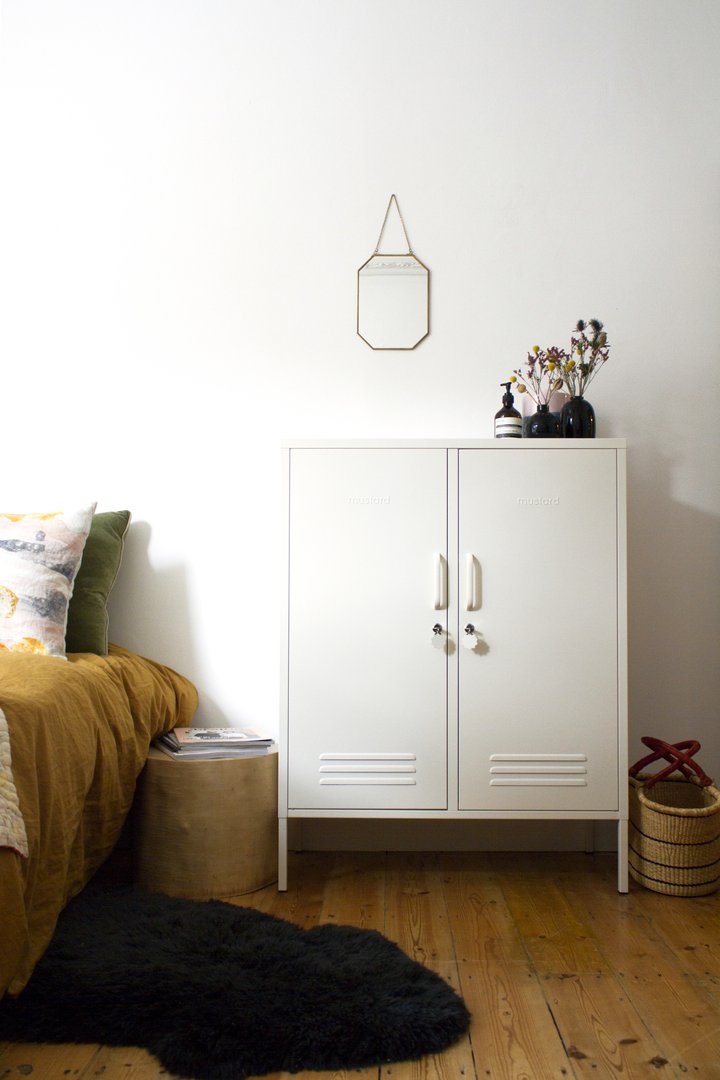 Mustard Made The Midi Locker in white beside a bed with a mirror hanging above it