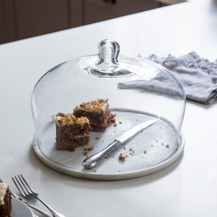 Glass cake stand with dessert and utensils on a kitchen counter