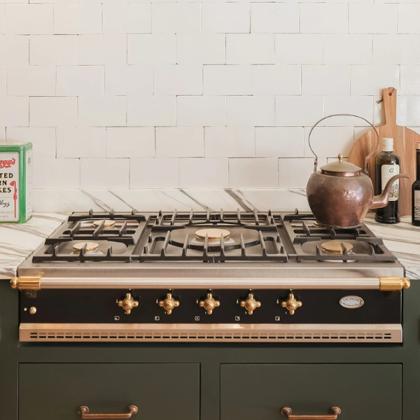 lacanche hob with stainless steel cooktop and brass knobs embedded indark green carpentry