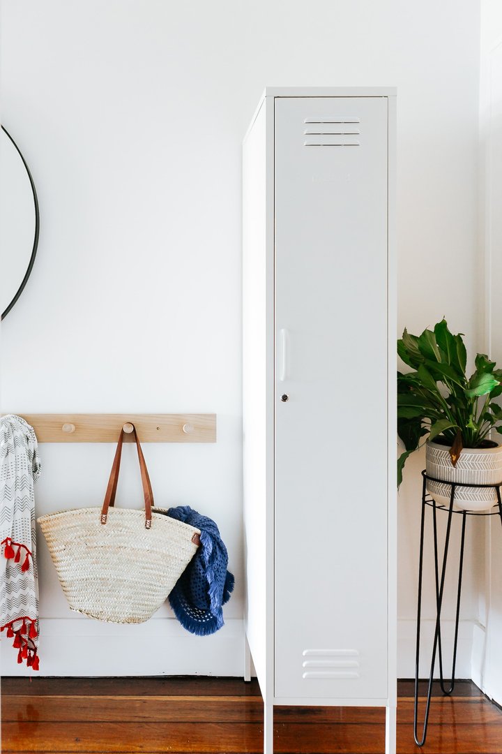 Mustard Made The Skinny Locker in white bbeside a hanging rack and a potted plant