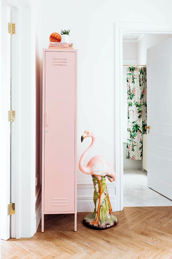 Mustard Made The Skinny Locker in pink beside a flamingo statue in the corner of a room