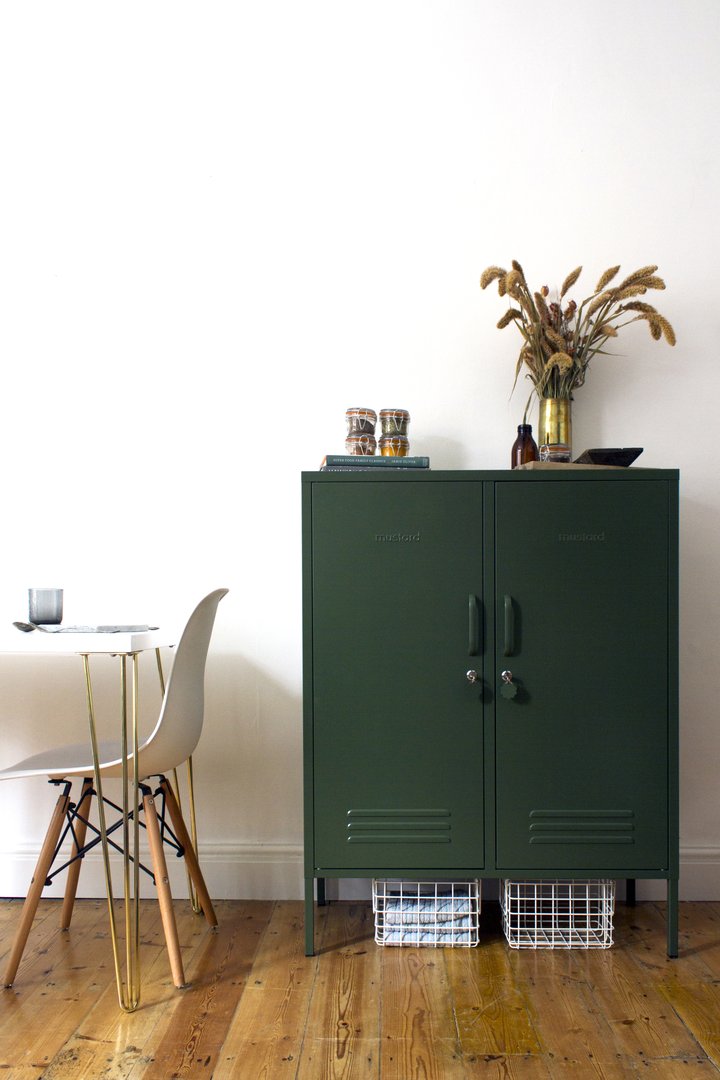 Mustard Made The Midi Locker in green with white baskets underneath beside a white table and chair