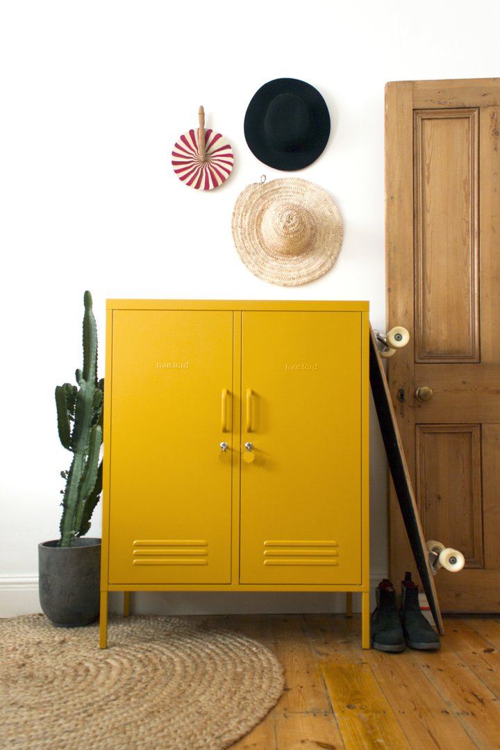 Mustard Made The Midi Locker in mustard with a cactus on one side and a skateboard leaning on the other side. There are also hats hanging above it.